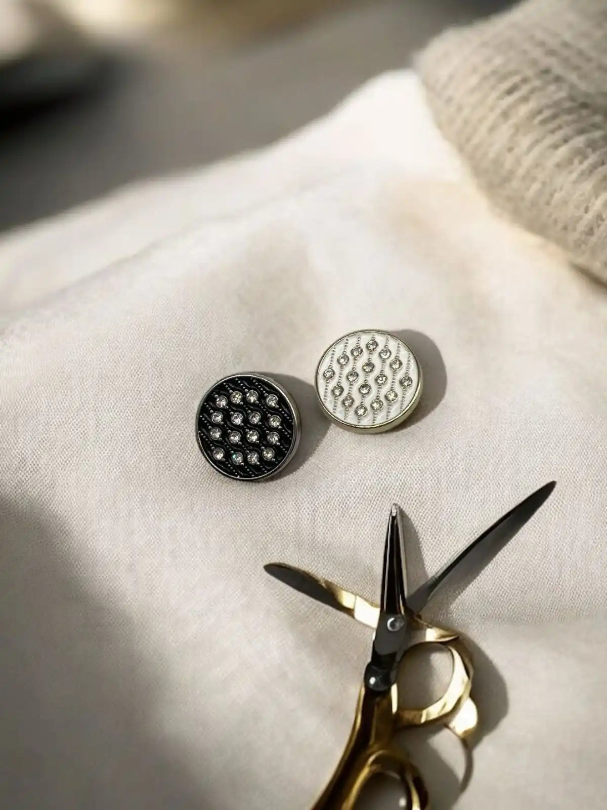 Two round, patterned sewing buttons in black and white, accompanied by gold-handled scissors.