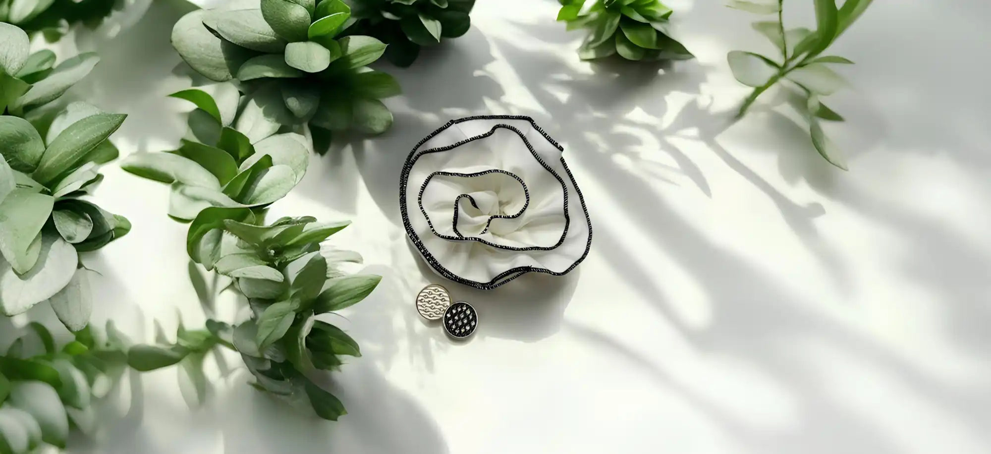 A fabric flower brooch with white petals outlined in black, accompanied by two small, round, decorative buttons—one silver, one black.