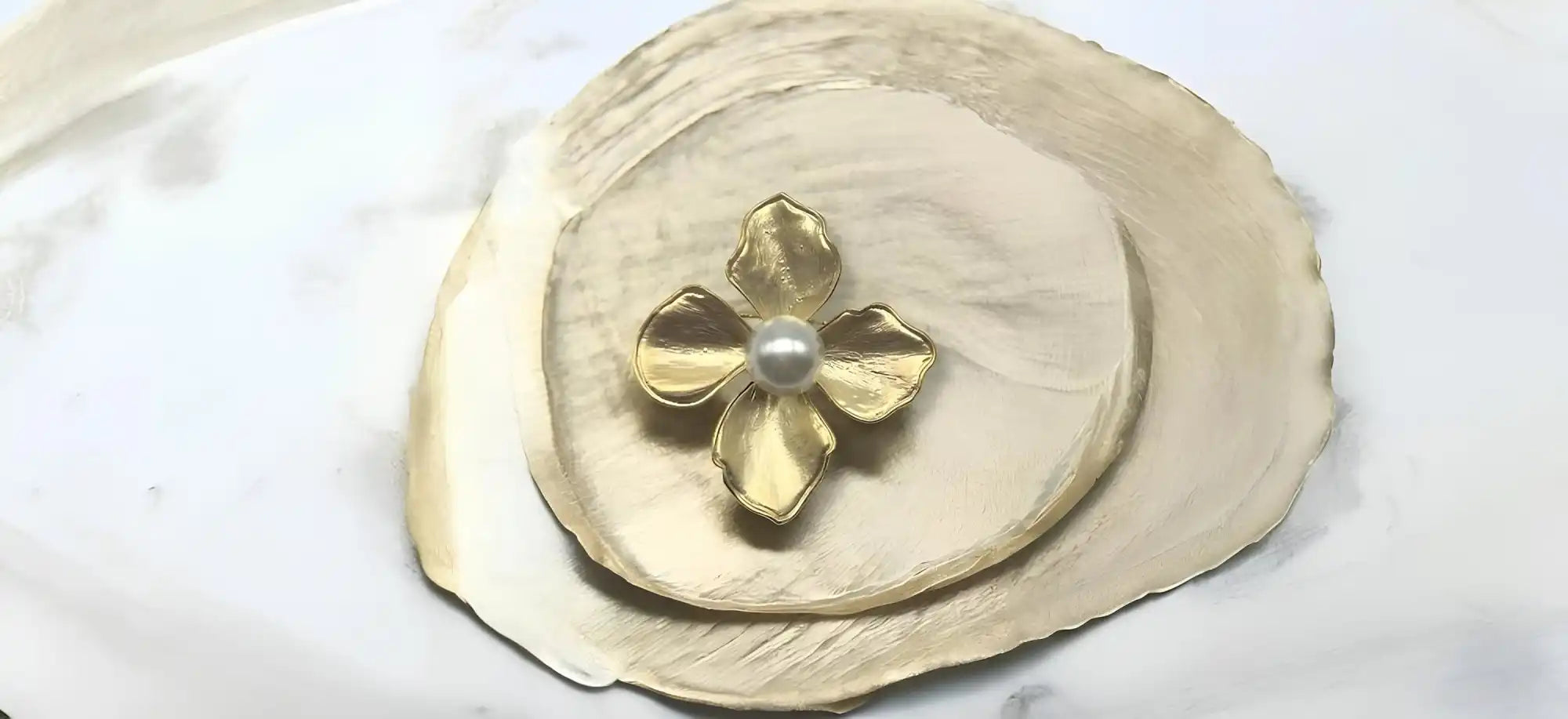 A natural shell dish with a central gold flower featuring a pearl.